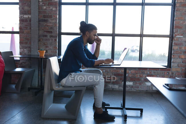 Thoughtful mixed race man sitting and using laptop in cafe. digital creatives on the go. — Stock Photo