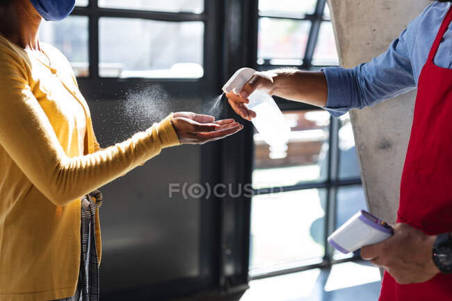 Midsection of diverse woman and man disinfecting hands. independent cafe, business during coronavirus covid 19 pandemic. — Stock Photo