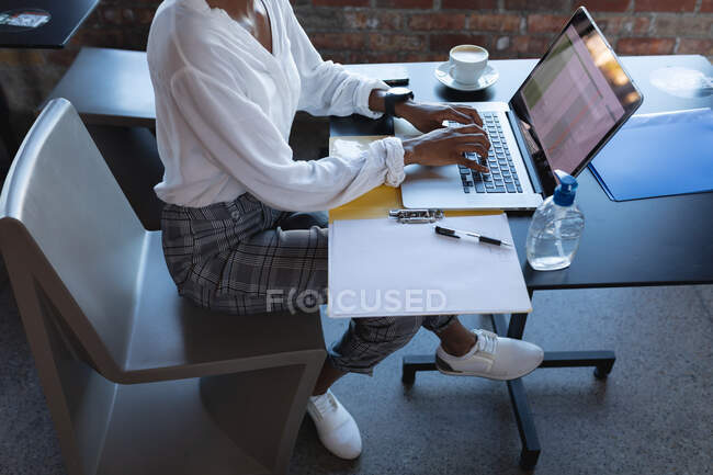 Baixa seção da mulher afro-americana usando laptop e trabalhando no café. criativos digitais em movimento. — Fotografia de Stock