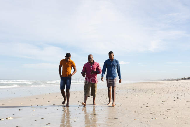 African american father and his two sons walking together at the beach. summer beach holiday and leisure concept. — Stock Photo