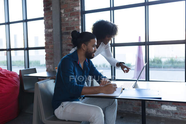 Усміхаючись, змішаний расовий чоловік і афро-американська жінка використовують ноутбук у кафе. Цифрові креативи у русі. — стокове фото