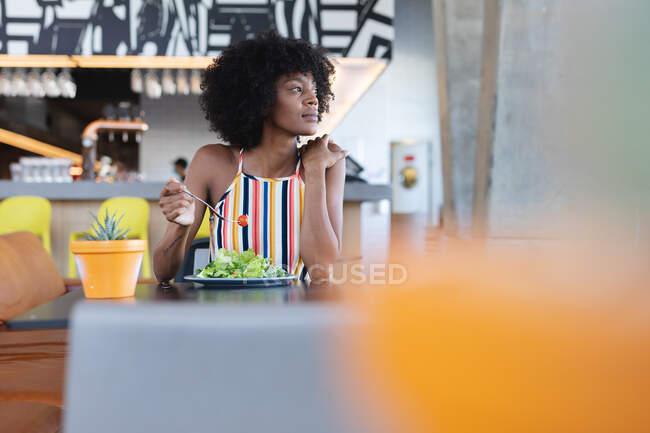 Mulher afro-americana sentada à mesa e a comer no restaurante. café independente, pequeno negócio bem sucedido. — Fotografia de Stock
