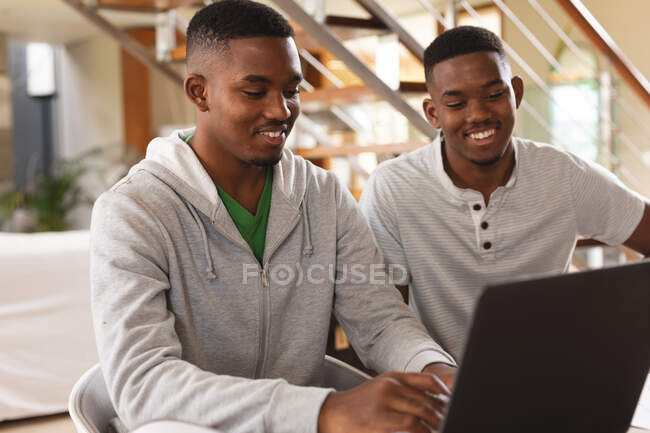 Hermanos afroamericanos sonriendo mientras usan el portátil en casa. aprendizaje a distancia y concepto de educación en línea - foto de stock