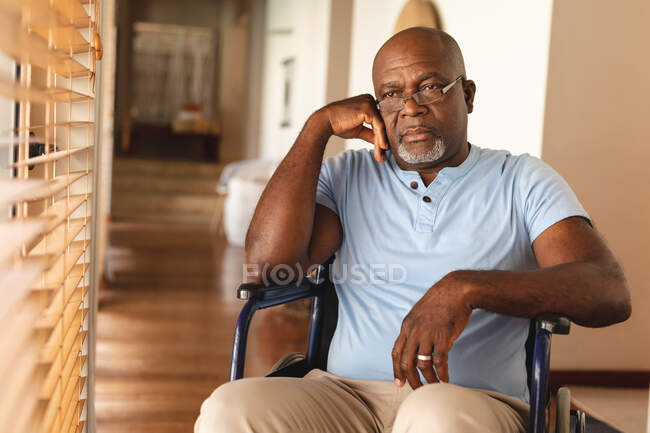 Hombre mayor afroamericano discapacitado estresado sentado en la silla de ruedas en casa. retiro y soledad de ancianos concepto - foto de stock