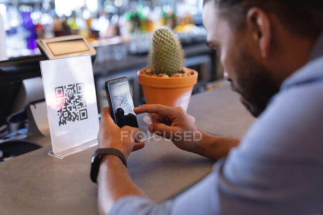 Uomo razza mista utilizzando smartphone e la lettura di codice QR in caffè. caffè indipendente, piccola impresa di successo. — Foto stock