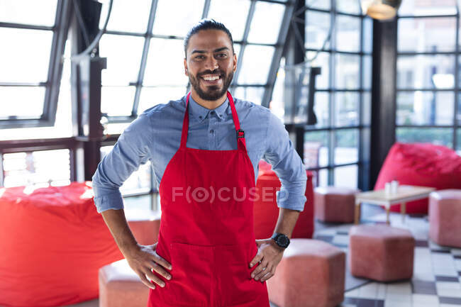 Smiling mixed race male barista wearing apron in cafe and looking at camera. independent cafe, small successful business. — Stock Photo