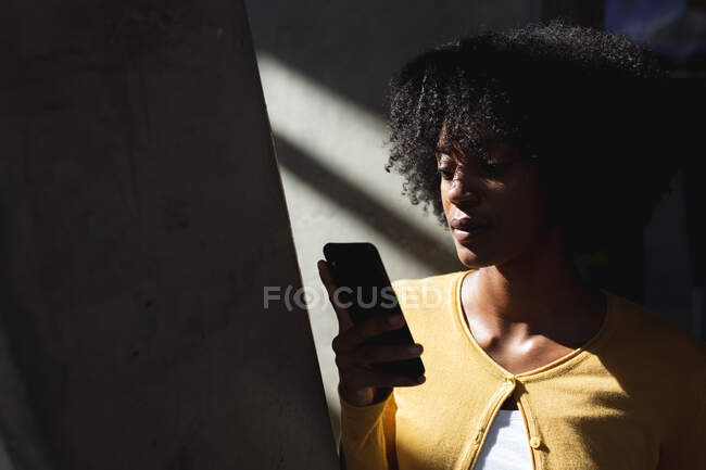 Porträt einer afrikanisch-amerikanischen Frau mit Smartphone im kontrastreichen Interieur. Digitale Kreative unterwegs. — Stockfoto