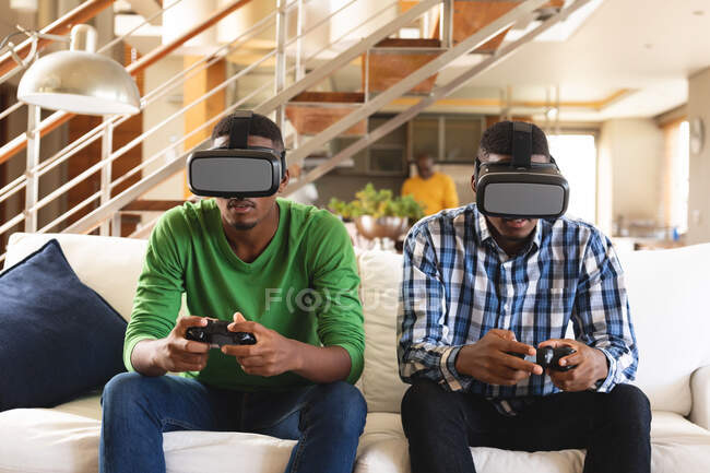 Frères afro-américains portant un casque vr jouer à des jeux vidéo tout en étant assis sur le canapé à la maison. concept de technologie de jeu et de divertissement — Photo de stock