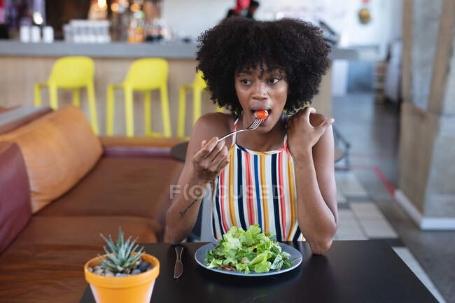 African american woman sitting at table and eating in restaurant. independent cafe, small successful business. — Stock Photo
