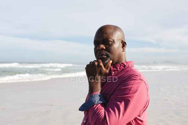 Afro-americano idoso com a mão no queixo em pé na praia. verão praia férias e lazer conceito. — Fotografia de Stock