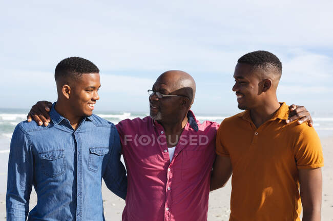 Père afro-américain et ses deux fils souriant tout en se tenant à la plage. vacances à la plage d'été et concept loisirs. — Photo de stock