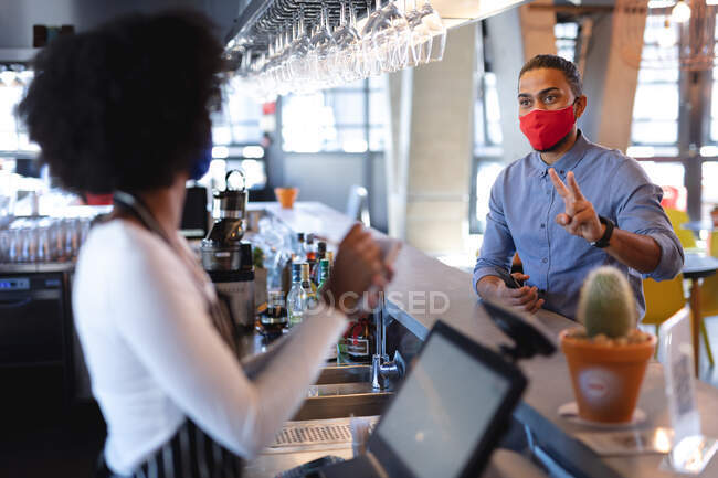 Змішана раса чоловічого клієнта в масці обличчя, розміщення порядку для африканського американського жіночого бариста. Незалежна кава, бізнес під час коронавірусної ковини 19 пандемії. — стокове фото