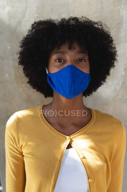 Portrait de femme afro-américaine portant un masque facial regardant la caméra. créatifs numériques sur la route pendant coronavirus covid 19 pandémie. — Photo de stock