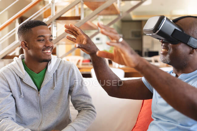 Jeune homme afro-américain enseignant à son père comment utiliser un casque vr à la maison. concept de technologie familiale et de divertissement — Photo de stock