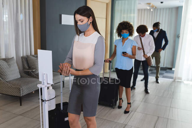 Diversas mulheres de negócios e homens de negócios em pé na fila para desinfectar as mãos no lobby do hotel. hotel de viagens de negócios durante coronavírus covid 19 pandemia. — Fotografia de Stock