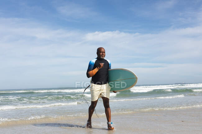 Afrikanischer älterer Herr mit Surfbrett, der in Richtung Strand läuft. Sommer-Strandurlaub und Freizeitkonzept. — Stockfoto