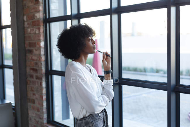 Donna afroamericana in piedi, che tiene la penna e pensa nel bar. creativi digitali in movimento. v — Foto stock