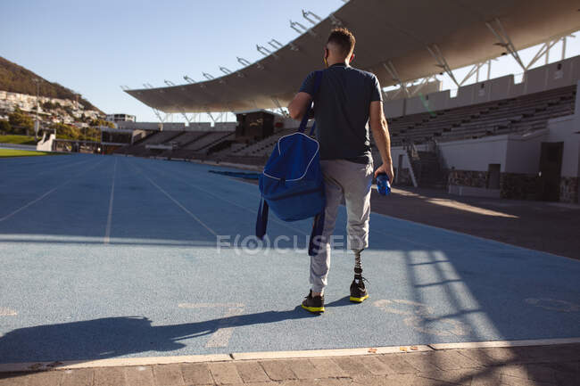 Vue arrière d'un athlète masculin caucasien avec une jambe prothétique debout sur un terrain de sport. concept de sport paralympique — Photo de stock