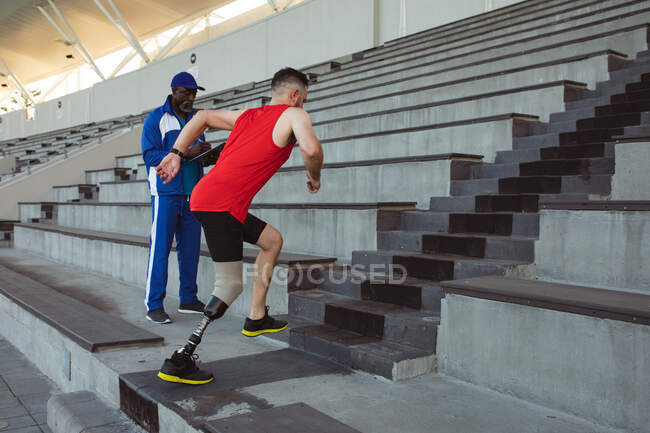 Кавказский спортсмен с протезной ногой карабкается по лестнице стадиона. Концепция паралимпийских игр — стоковое фото