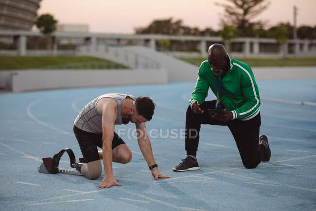 Caucasian male athlete with prosthetic leg in starting position for running on the track. paralympic sport concept — Stock Photo