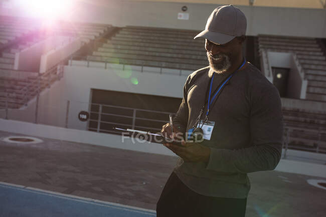 Entrenador masculino afroamericano con portapapeles tomando notas en pista de atletismo en el estadio. concepto de deporte paralímpico - foto de stock