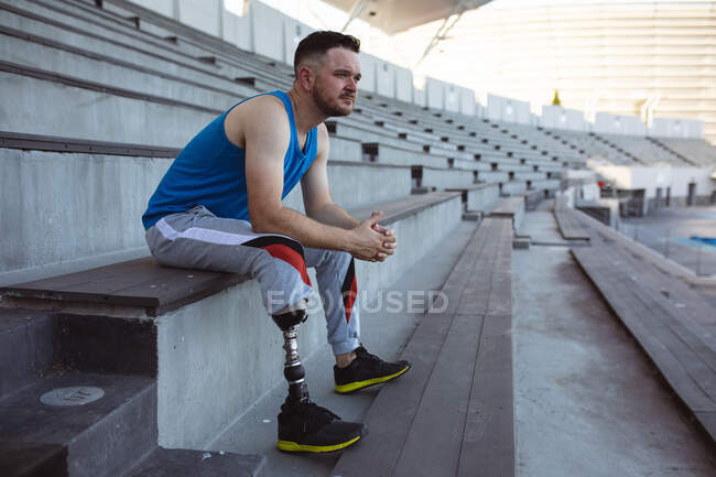 Кавказский спортсмен с протезной ногой сидит на сиденьях на стадионе. Концепция паралимпийских игр — стоковое фото