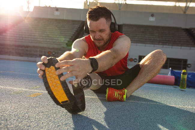 Caucasian male athlete with prosthetic leg performing stretching exercise on running track. paralympic sport concept — Stock Photo