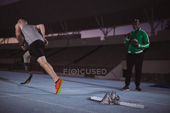 Caucasian male athlete with prosthetic leg running on the track at night. paralympic sport concept — Stock Photo