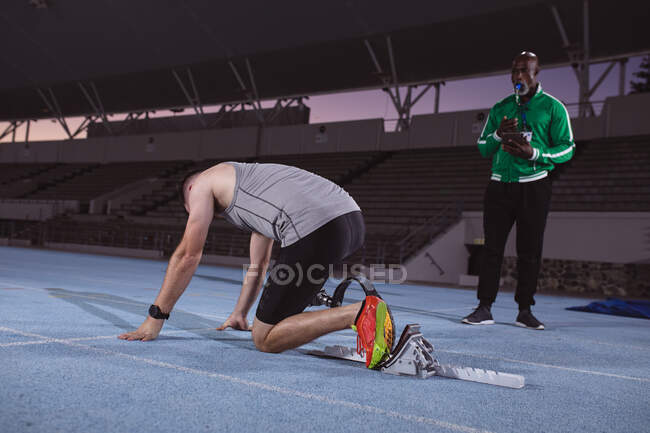 Athlète masculin caucasien avec prothèse de jambe en position de départ pour courir sur la piste la nuit. concept de sport paralympique — Photo de stock