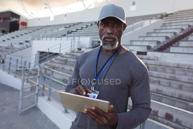 Retrato del entrenador afroamericano que sostiene el portapapeles parado en el estadio. concepto de deporte paralímpico - foto de stock