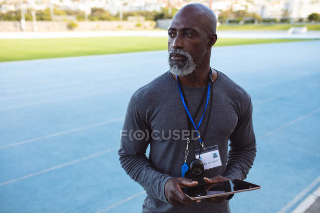 Entrenador masculino sénior afroamericano sosteniendo tableta digital de pie en el estadio. concepto de deporte paralímpico - foto de stock