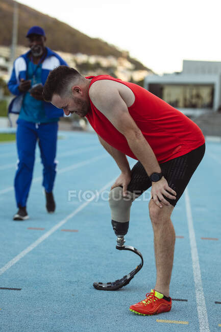 Atleta maschio caucasico stanco con gamba protesica che si prende una pausa dalla corsa in pista. concetto di sport paralimpico — Foto stock
