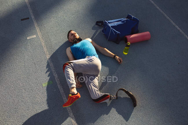 Atleta masculino caucásico con prótesis de pierna realizando ejercicio de estiramiento en pista de atletismo. concepto de deporte paralímpico - foto de stock