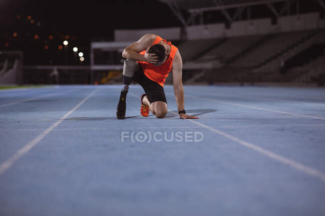 Разочарованный кавказский спортсмен с протезной ногой с рукой на голове, сидящий на беговой дорожке. Концепция паралимпийских игр — стоковое фото