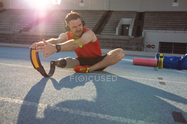 Atleta masculino caucásico con prótesis de pierna realizando ejercicio de estiramiento en pista de atletismo. concepto de deporte paralímpico - foto de stock