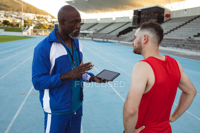 African american male coach instructing caucasian male athlete with prosthetic leg on running track. paralympic sport concept — Stock Photo