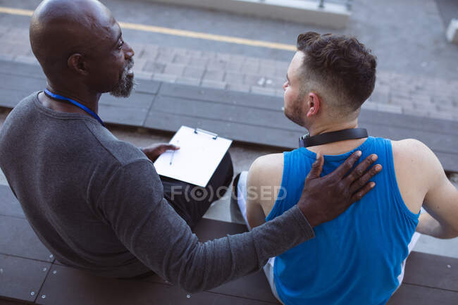 African american male coach supporting caucasian male athlete with prosthetic leg in the stadium. paralympic sport concept — Stock Photo