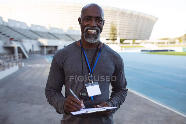 Portrait of african american male coach holding clipboard smiling while standing in the stadium. paralympic sport concept — Stock Photo