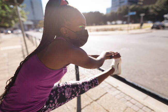 Жирна афро-американська жінка в масці, що розтягується в місті. Здоровий активний спосіб життя і пристосованість на відкритому повітрі під час коронавірусу covid 19 пандемії. — стокове фото