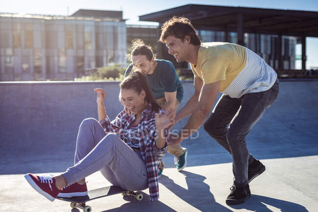 Drei glückliche kaukasische Freundinnen und Freunde, die mit Skateboard in der Sonne spielen. Im Sommer im städtischen Skatepark abhängen. — Stockfoto