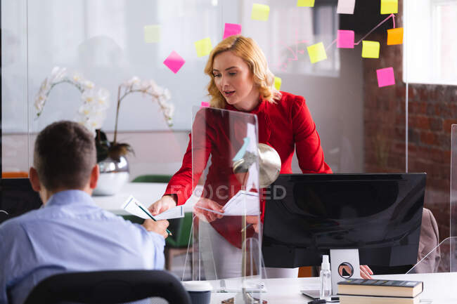 Mujer caucásica pasando un documento a su colega en la oficina. negocio, profesionalidad, concepto de oficina y trabajo en equipo - foto de stock