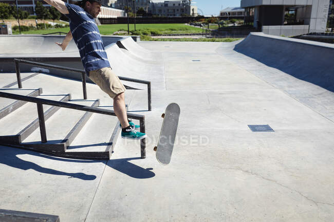 Белый мужчина падает со скейтборда в солнечный день. тусоваться в городском скейтпарке летом. — стоковое фото