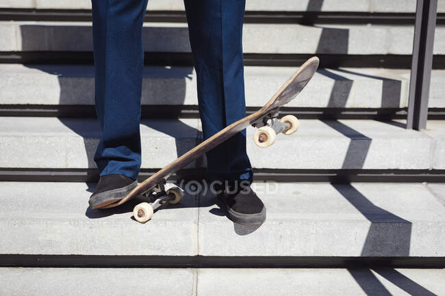 Низкая часть бизнесмена, стоящего на скейтборде под солнцем. тусоваться в городском скейтпарке летом. — стоковое фото
