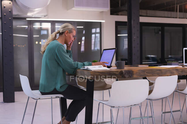 Kaukasische junge Frau benutzt Laptop, während sie im modernen Büro arbeitet. Business, Professionalität und Bürokonzept — Stockfoto