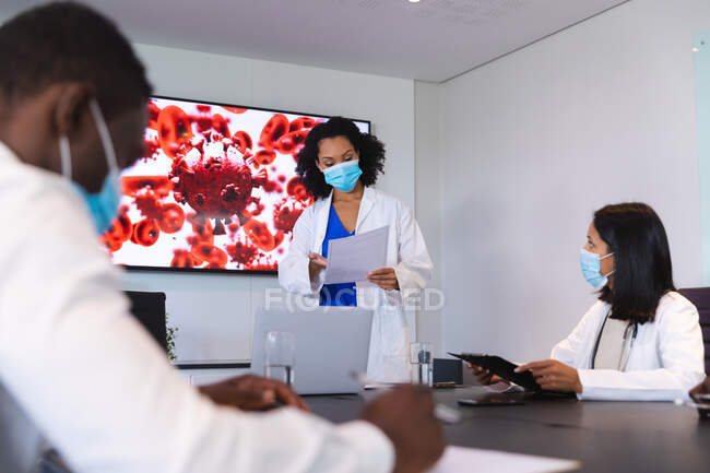 African american female doctor wearing face mask giving presentation to team of doctors. healthcare and medical research during covid 19 pandemic — Stock Photo