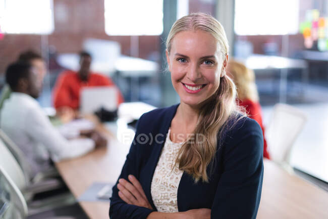 Ritratto di donna caucasica con le braccia incrociate sorridente mentre si trova in un ufficio moderno. business, professionalità e concetto di ufficio — Foto stock