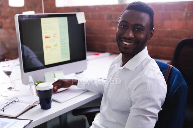 Portrait d'un homme afro-américain souriant assis sur son bureau au bureau moderne. affaires, professionnalisme et concept de bureau — Photo de stock