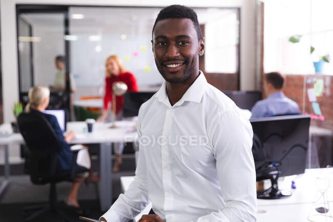 Ritratto di uomo afroamericano sorridente mentre si trova in un ufficio moderno. business, professionalità e concetto di ufficio — Foto stock