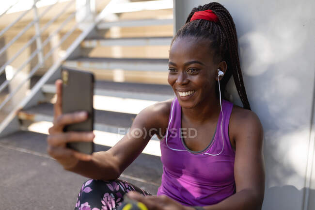 Sorrindo apto afro-americano mulher tomando selfie com smartphone durante o exercício na cidade. estilo de vida ativo urbano saudável e aptidão ao ar livre. — Fotografia de Stock