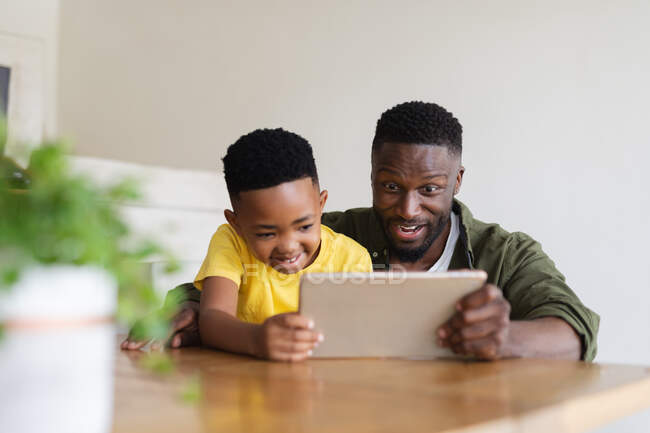 Африканський американський батько і син сидять за столом, користуючись планшетом і посмішкою. вдома в ізоляції під час карантину.. — стокове фото